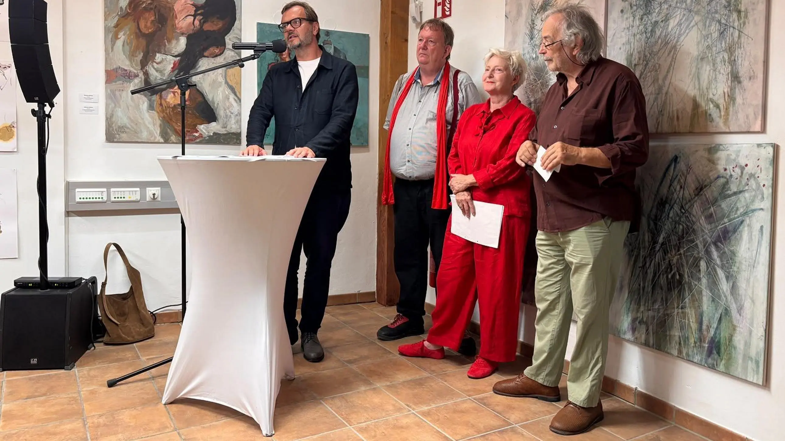 Vier Personen stehen vor Kunstwerken, eine davon spricht ins Mikrofon.