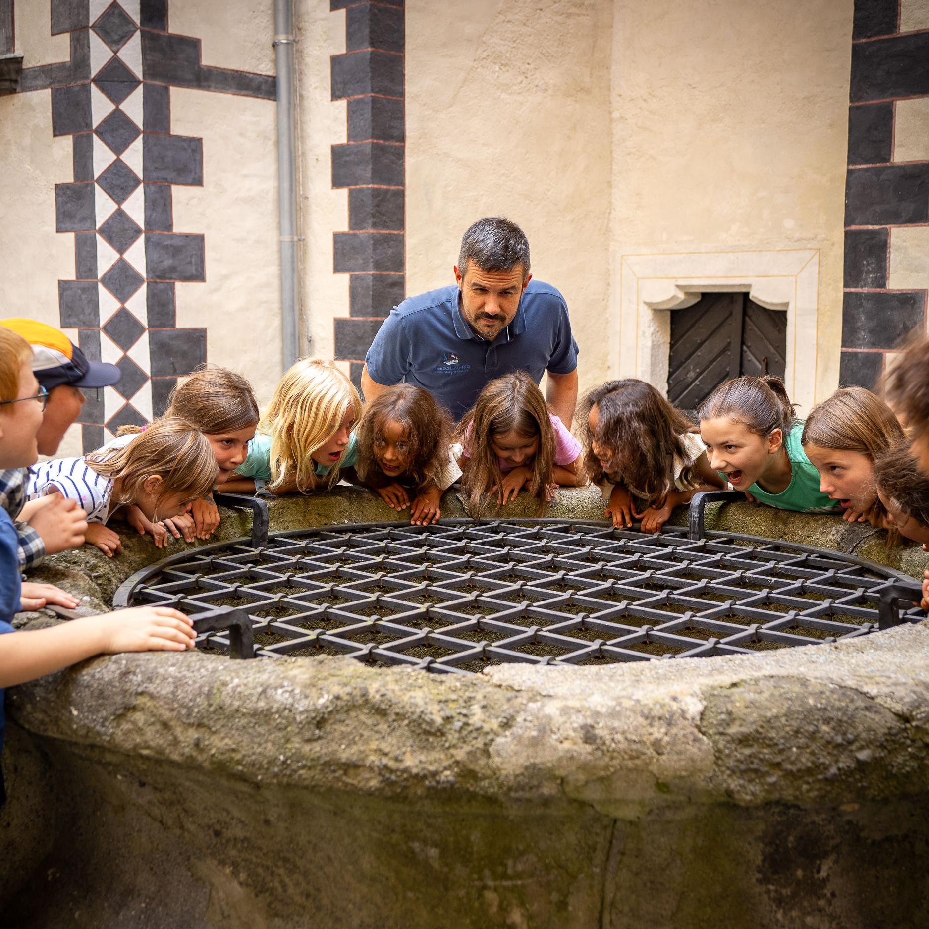Eine Gruppe von Kindern und ein Mann stehen rund um einen Brunnen und schauen hinein